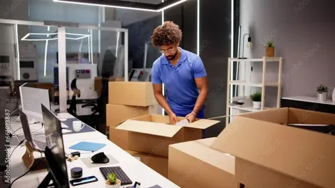 A professional packing cardboard boxes inside a modern workspace during an office moving process