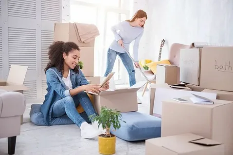 Two women packing household items into cardboard boxes in a living room, illustrating different Types of Moving