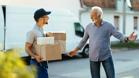 Senior citizens moving houses comfortably with the help of professional senior relocation services, carrying packing boxes through the front door.