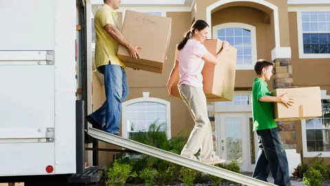 Professional residential moving service team carrying labeled boxes from a house into a moving truck.